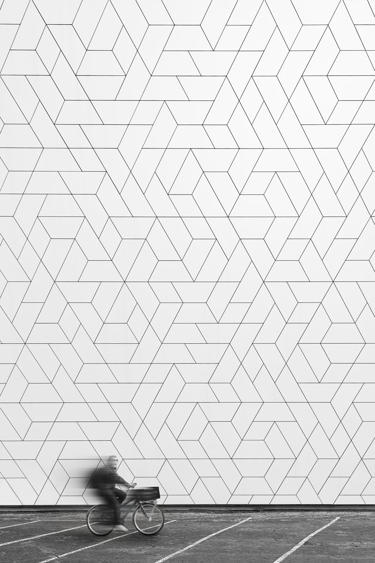 A black and white minimalist photograph of a cyclist riding past the geometric facade of the Eye Filmmuseum in Amsterdam. 