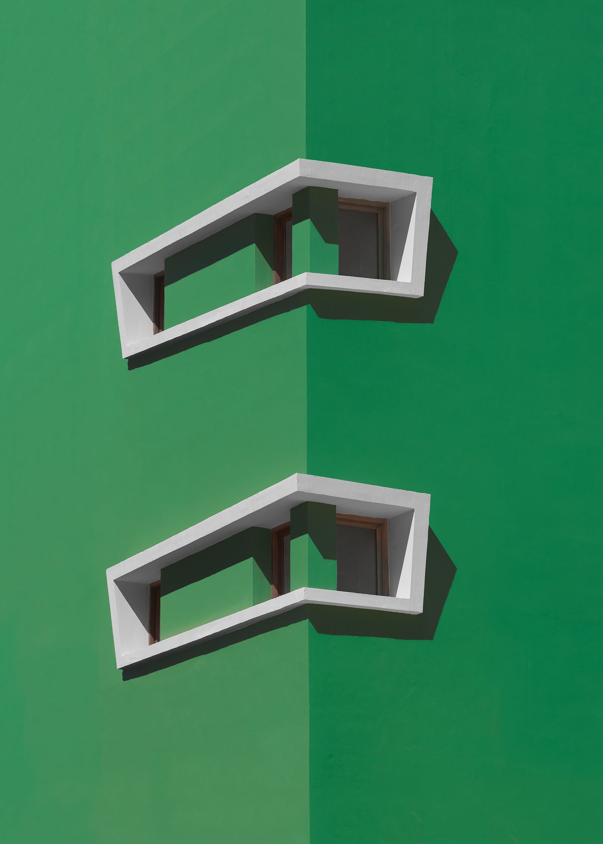 A minimalist architectural photograph of a vibrant green building corner featuring two white, corner windows casting sharp shadows. 