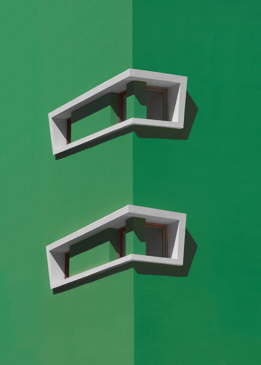 A minimalist architectural photograph of a vibrant green building corner featuring two white, corner windows casting sharp shadows. 