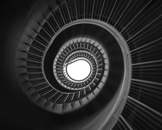 Black and white architectural photograph of a moving spiral staircase looking straight up toward a bright opening.